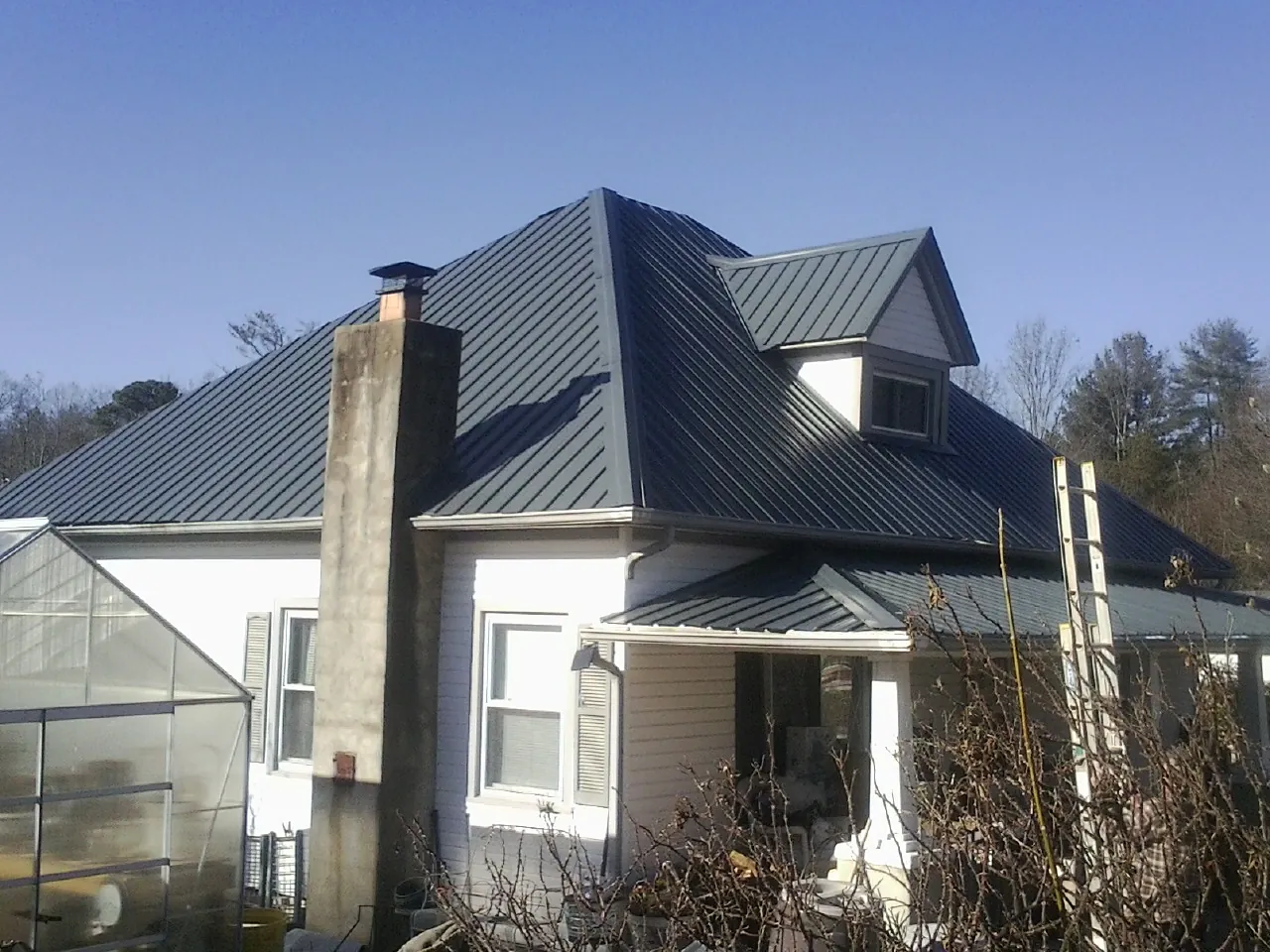 Dark blue standing seam metal roof on a white farmhouse with dormer — Slate & Tile Roof Repair by Roofing Brothers in Colo