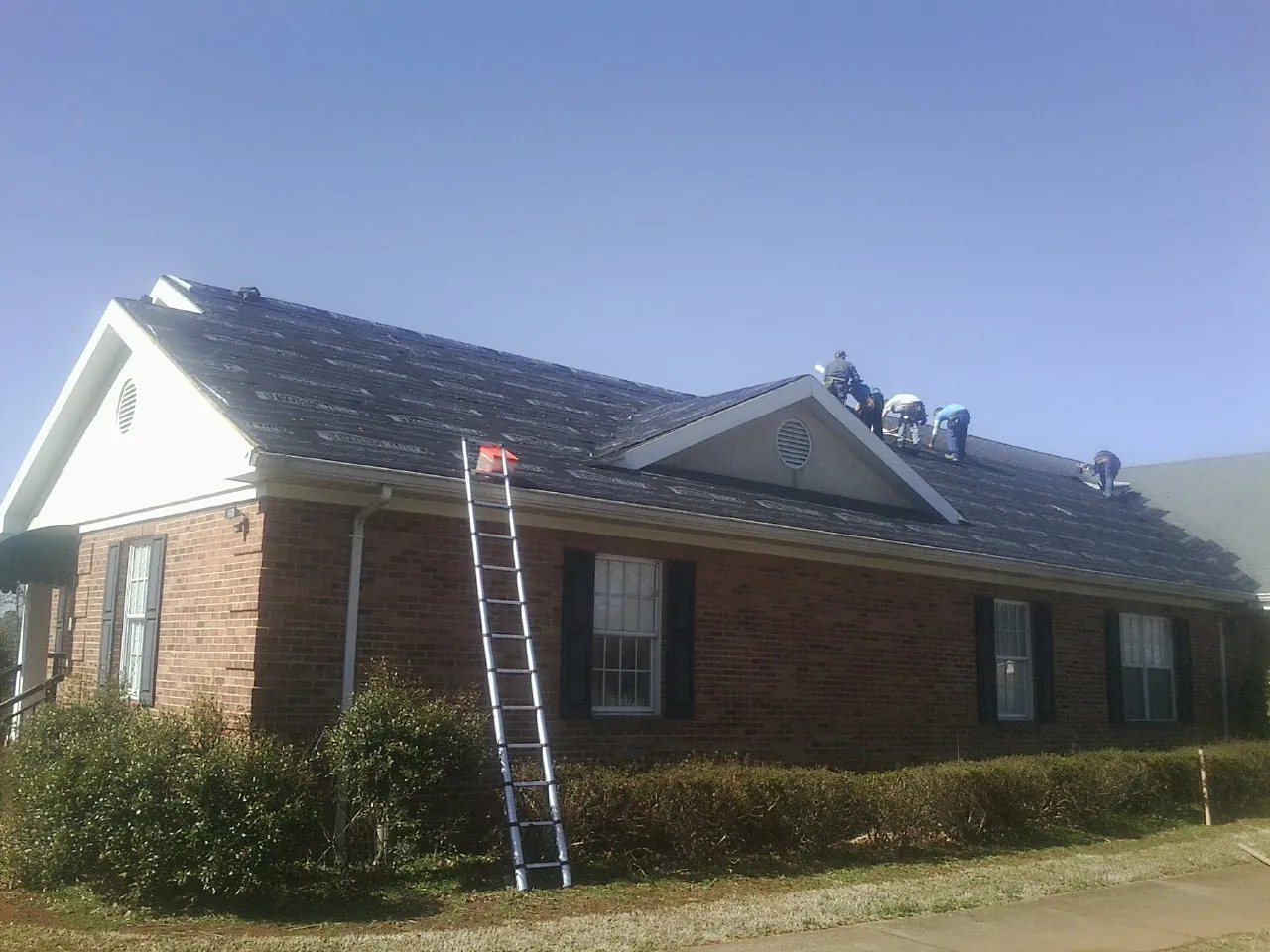 Crew tearing shingles off a brick ranch roof with a ladder set — Emergency Roof Repair work by our crew in Colo