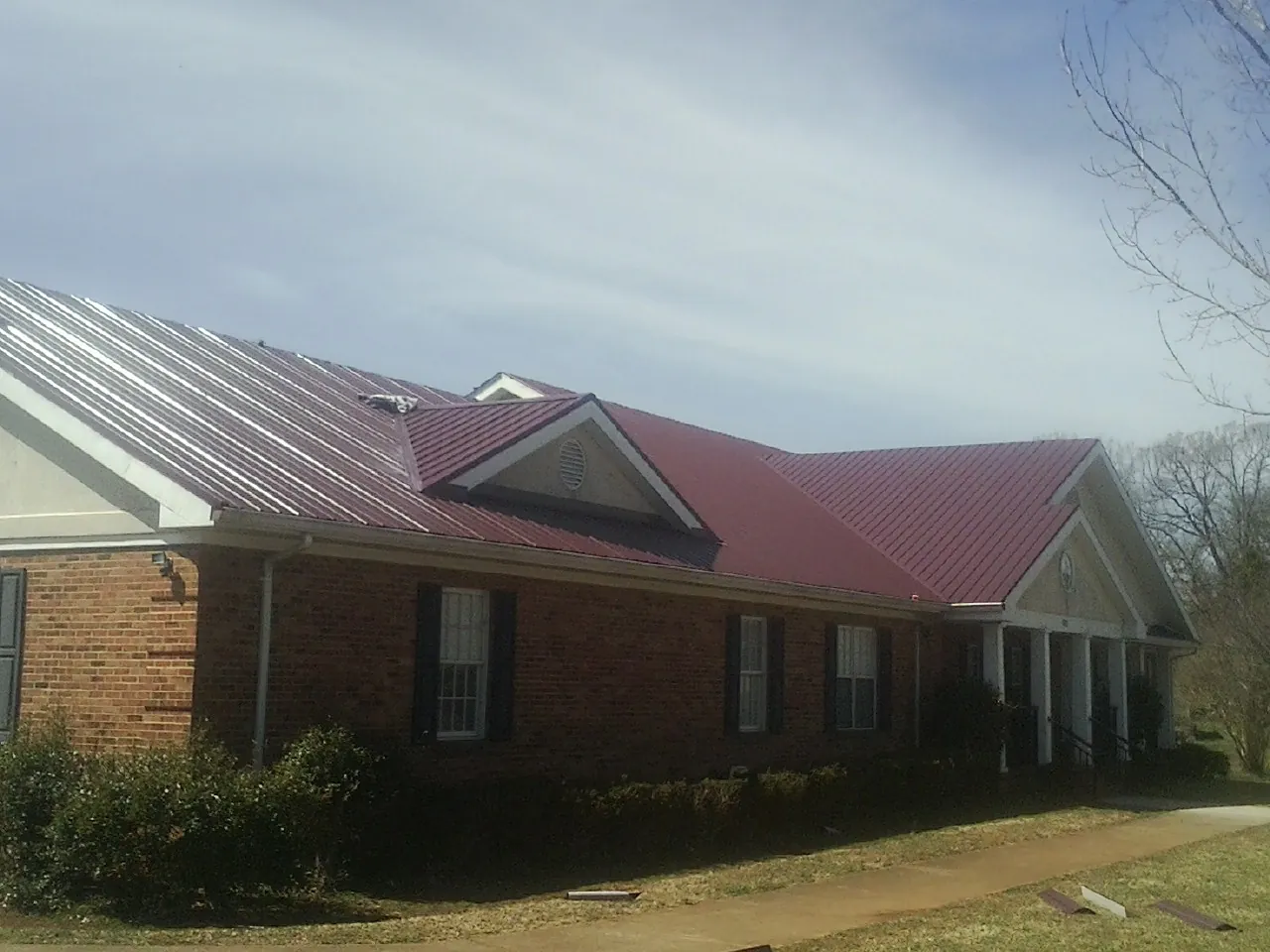 Red metal roof with gabled entries on a long brick building, from a Hail Damage Roof Repair job in Colo
