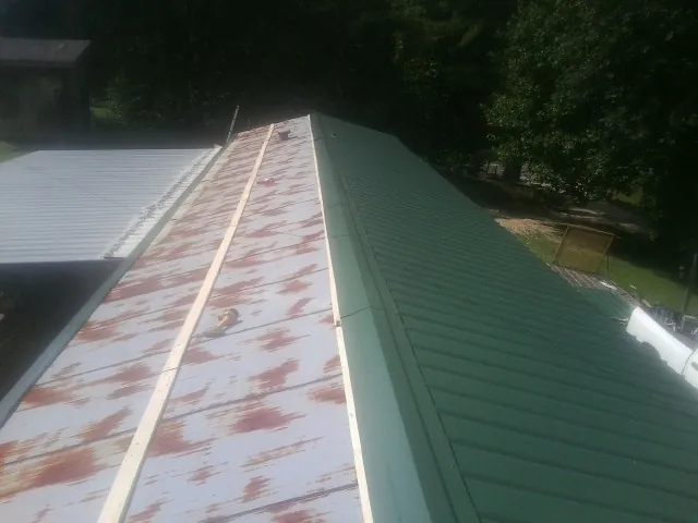 Old rusted panels beside newly installed green metal roofing — Wind Damage Roof Repair by Roofing Brothers in Colo