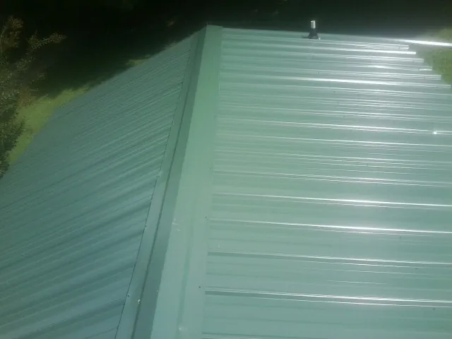 New green metal panels meeting at the ridge of a roof — Flat Roof Repair work by our crew in Colo