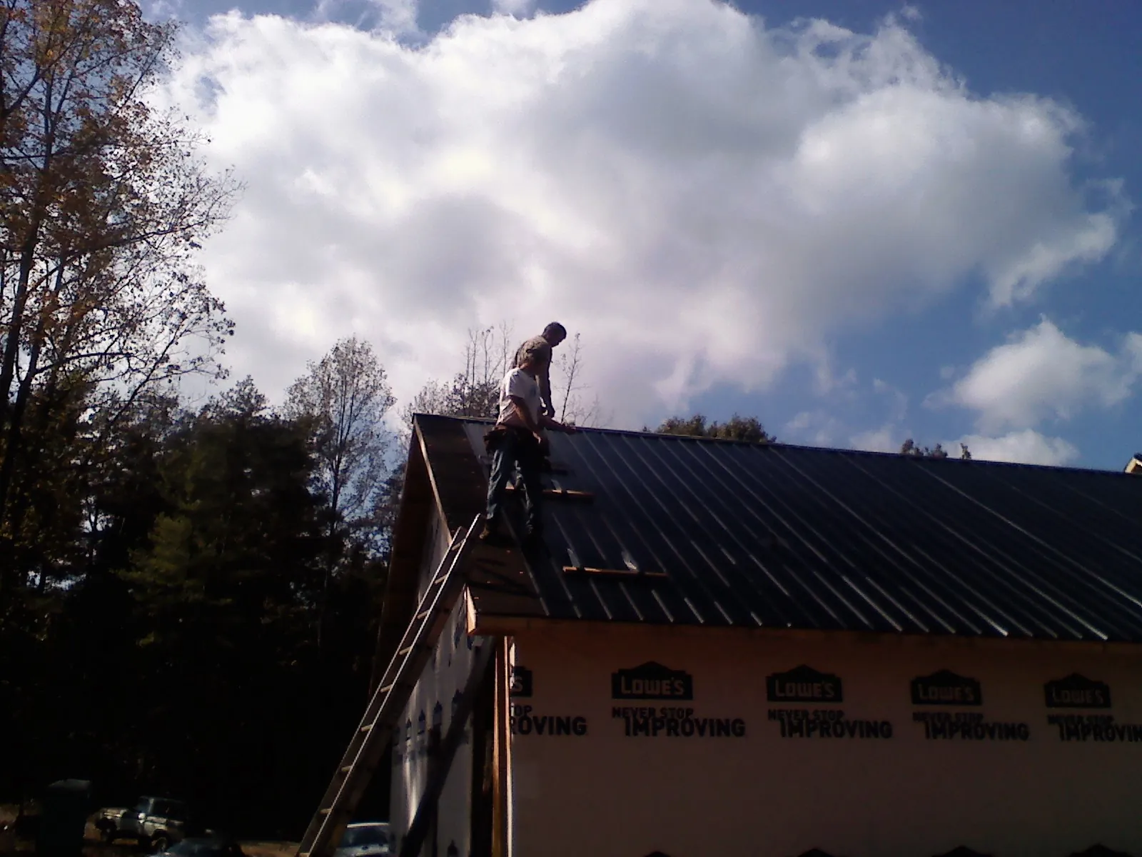 Roofer fastening dark metal panels high against a cloudy sky, from a Roof Inspection job in Colo