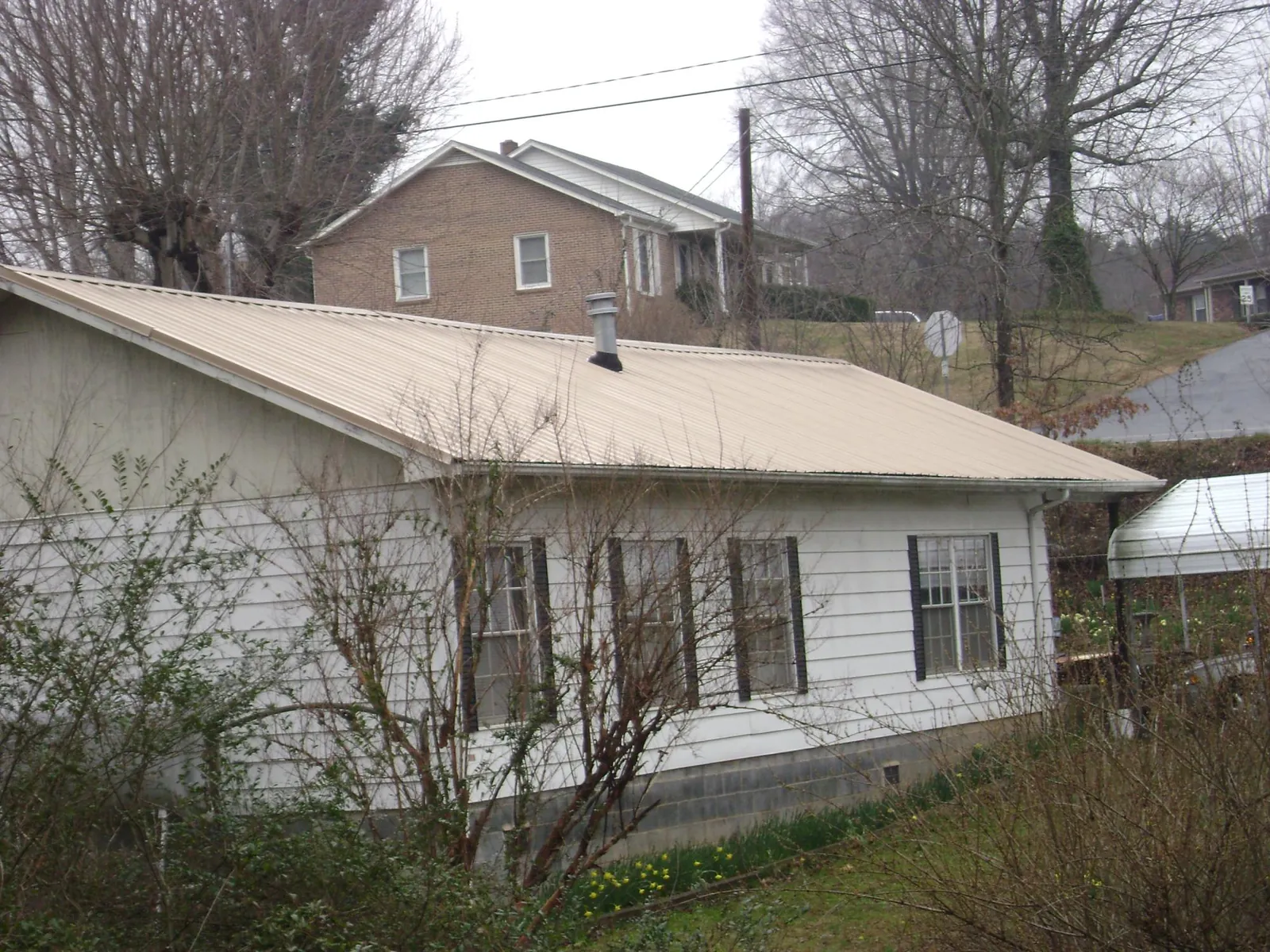 Tan metal roof on a white sided house set into a hillside — Commercial Roofing by Roofing Brothers in Colo