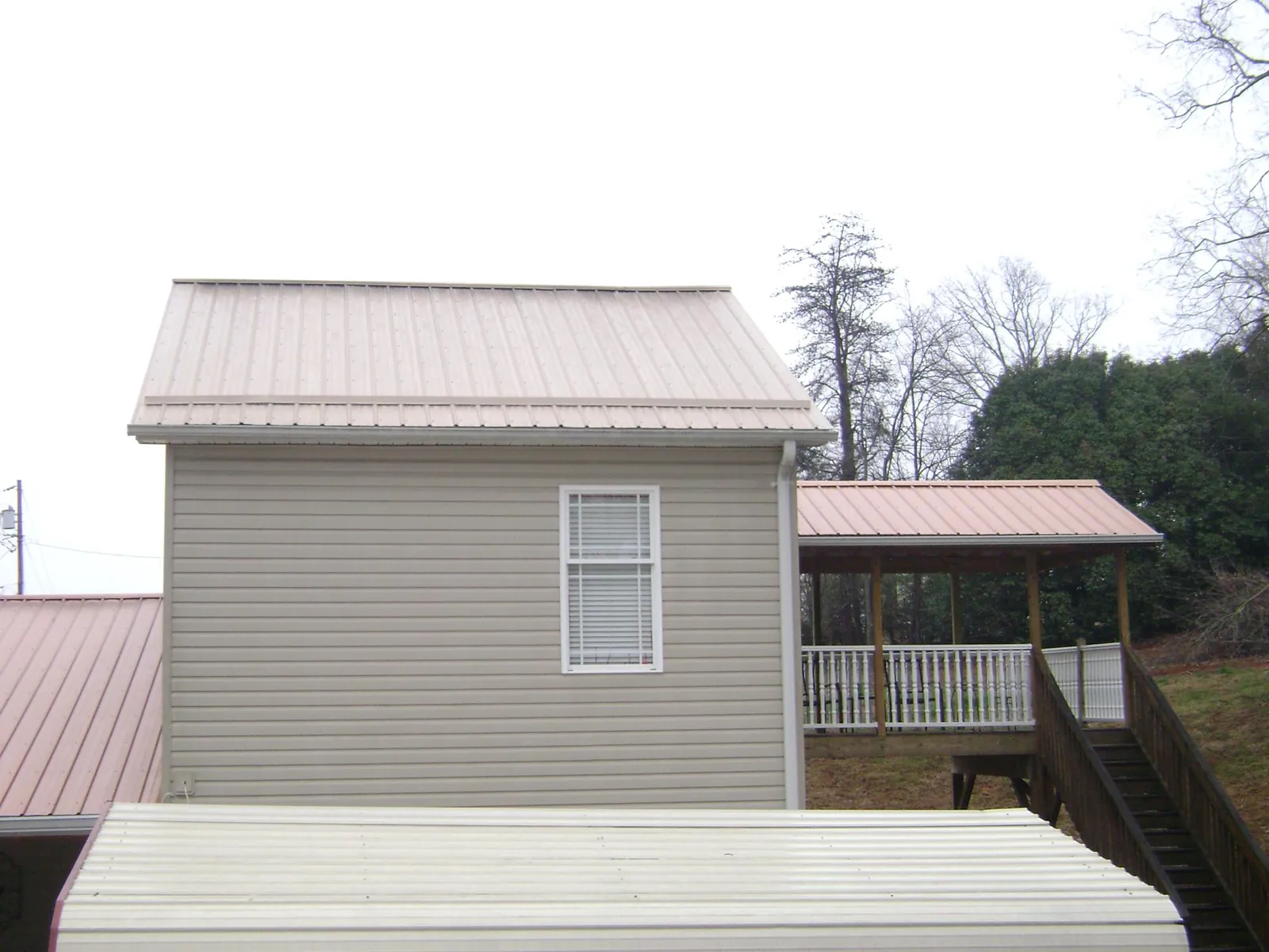 Tan metal roofs on a two story addition and attached porch, from a Roof Replacement job in Colo
